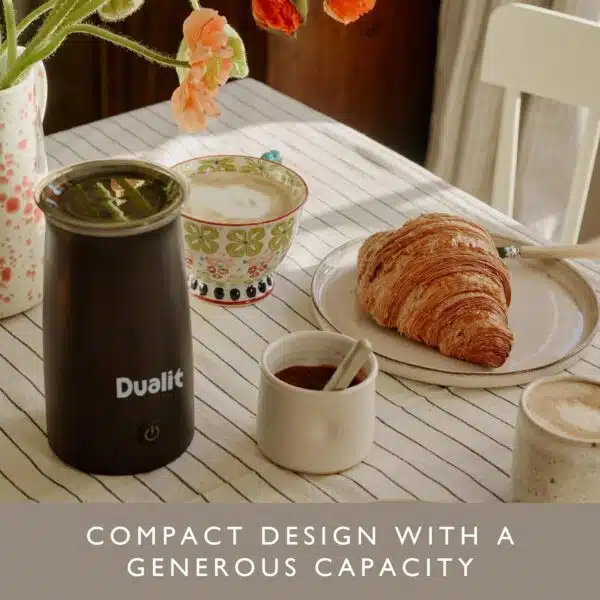 Dualit handheld milk frother on a breakfast table with a cup of frothy milk and pastries.