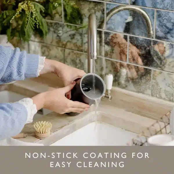 Hands cleaning Dualit handheld milk frother under tap, highlighting non-stick coating.