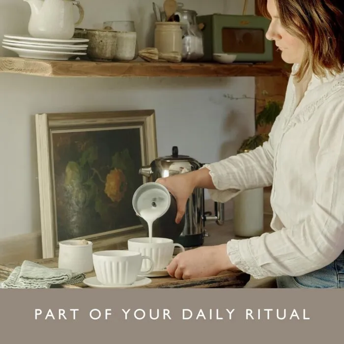 Woman Using Dualit Handheld Milk Frother to Pour Frothed Milk into a Cup in a Cozy Kitchen